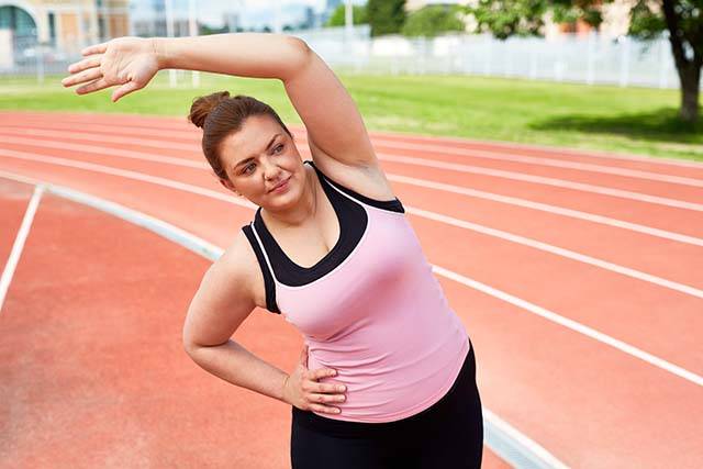A woman engaged in Sunrise Wellness Solution weight loss programs stretches on a running track.